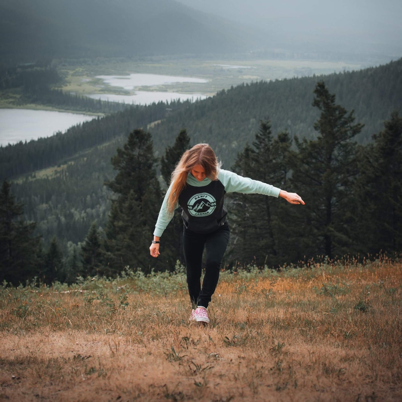 A woman walking through an alpine meadow with muted greens and warm tones